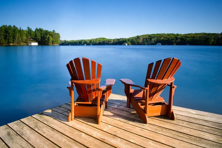 Two Adirondack chairs on a dock overlooking a blue lake